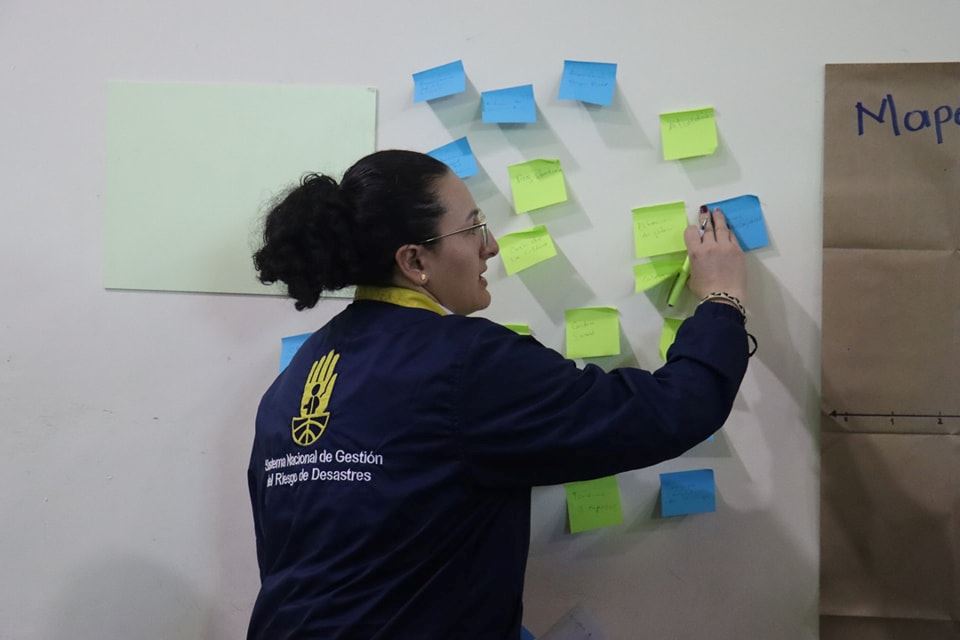 Mujer representante de la Unidad de la Gestión de Riesgos pega posit de colores con temas clave para identificar factores de riesgo geográfico en Cucunubá