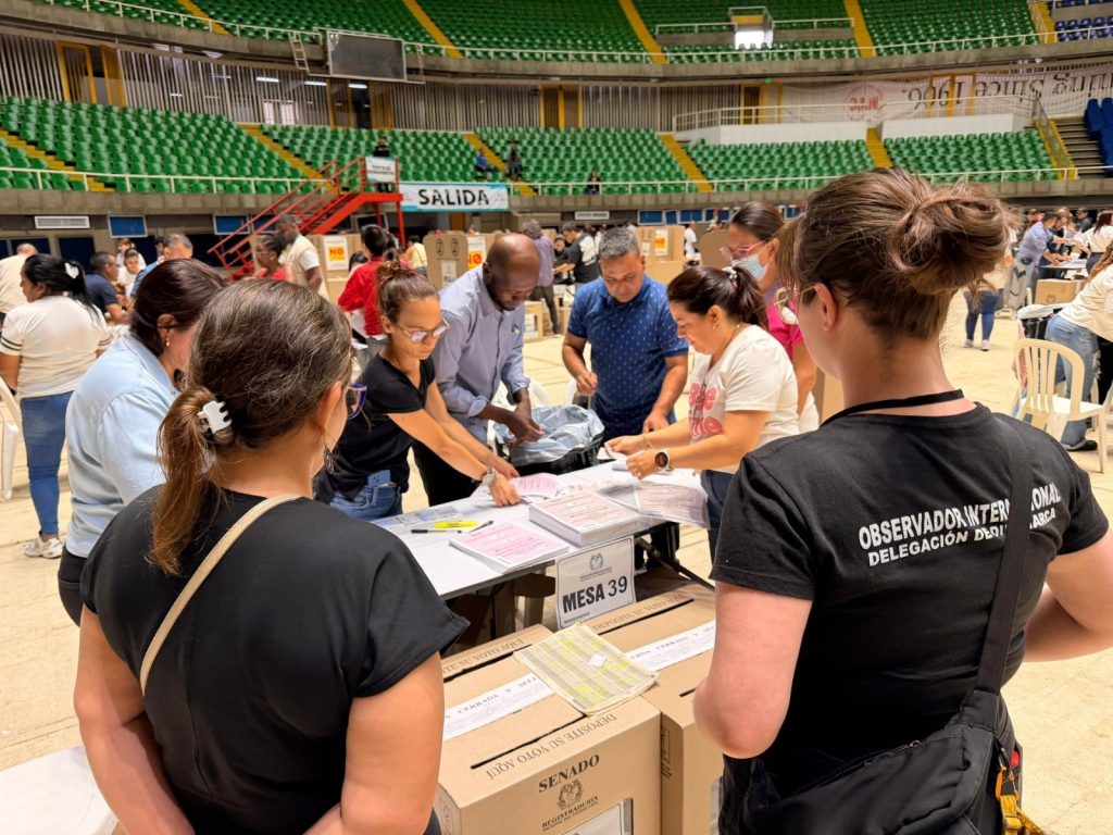 Grupo de personas al rededor de las mesas de votación.