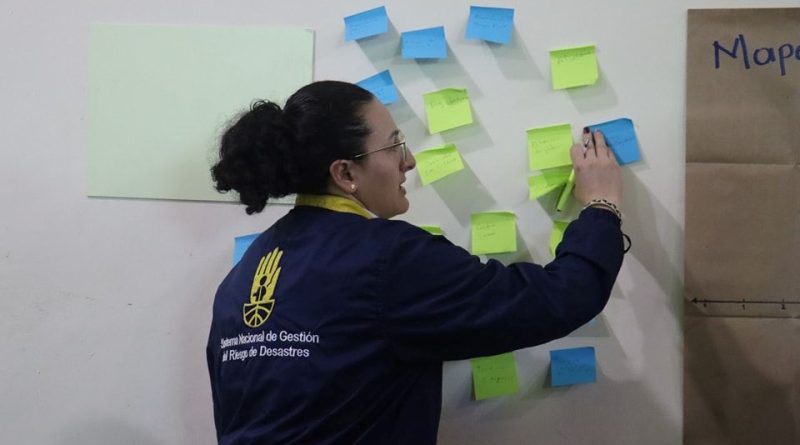 Mujer representante de la Unidad de la Gestión de Riesgos pega posit de colores con temas clave para identificar factores de riesgo geográfico en Cucunubá