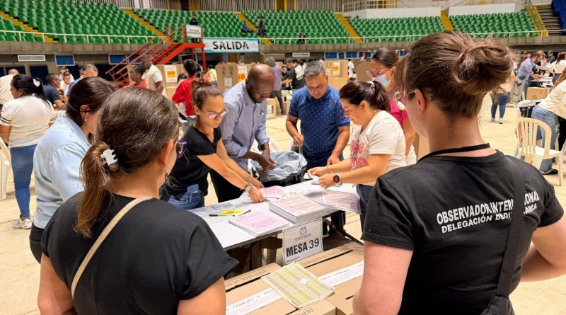 Grupo de personas al rededor de las mesas de votación.